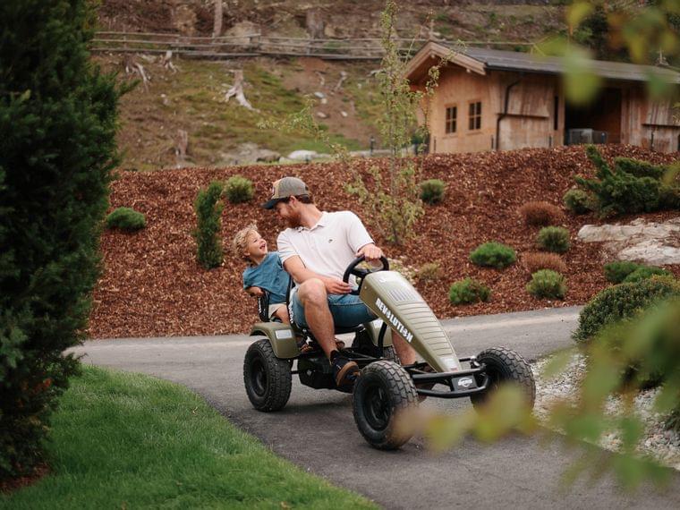 Adventure playground with go-karts, balance bikes and pedal vehicles Dad driving a go-kart with his child on a paved path at the playground