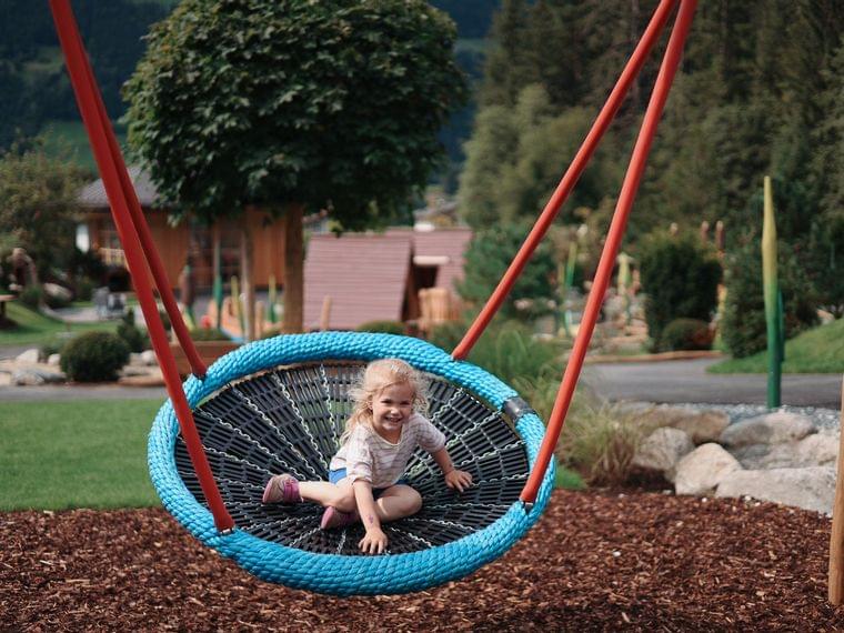 Nestschaukel am Abenteuerspielplatz vom Familienhotel Habachklause Kind schaukelt in einer runden Nestschaukel
